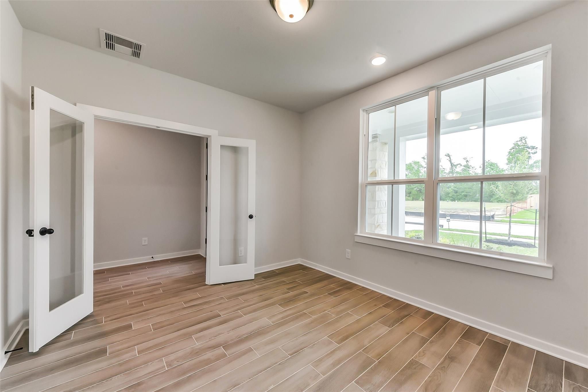Bright study with open glass French doors, hardwood-look tile floors, and large windows overlooking Sundance Cove greenery in Crosby, Texas