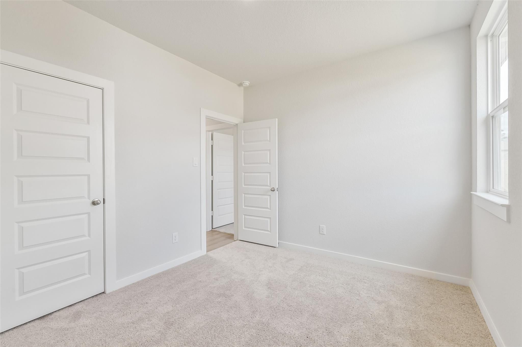 Bright secondary bedroom with beige carpet, white walls, and open door to en-suite bath in Davidson Homes The Frio G, Cleveland, Texas