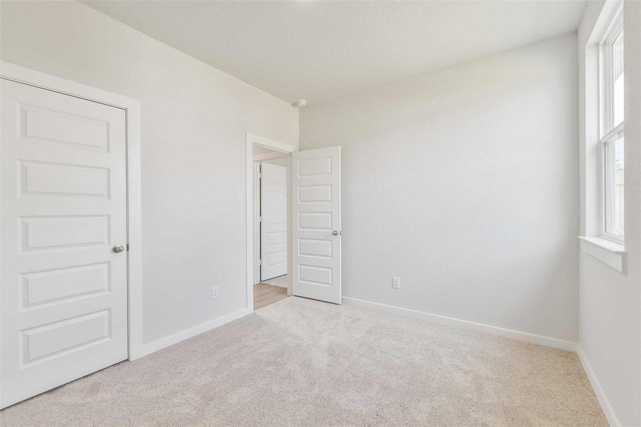 Bright secondary bedroom with beige carpet, white walls, and open door to en-suite bath in Davidson Homes The Frio G, Cleveland, Texas
