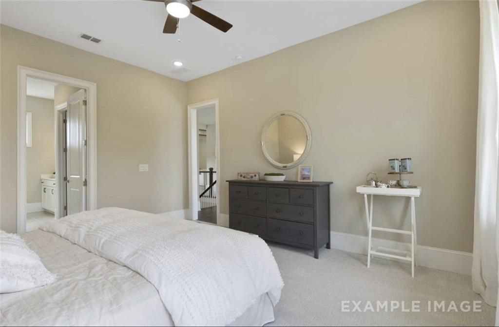 Elegant master bedroom with king bed, dark dresser, vanity mirror, and en-suite bath in Davidson Homes The Seaside A, Woodstock, GA