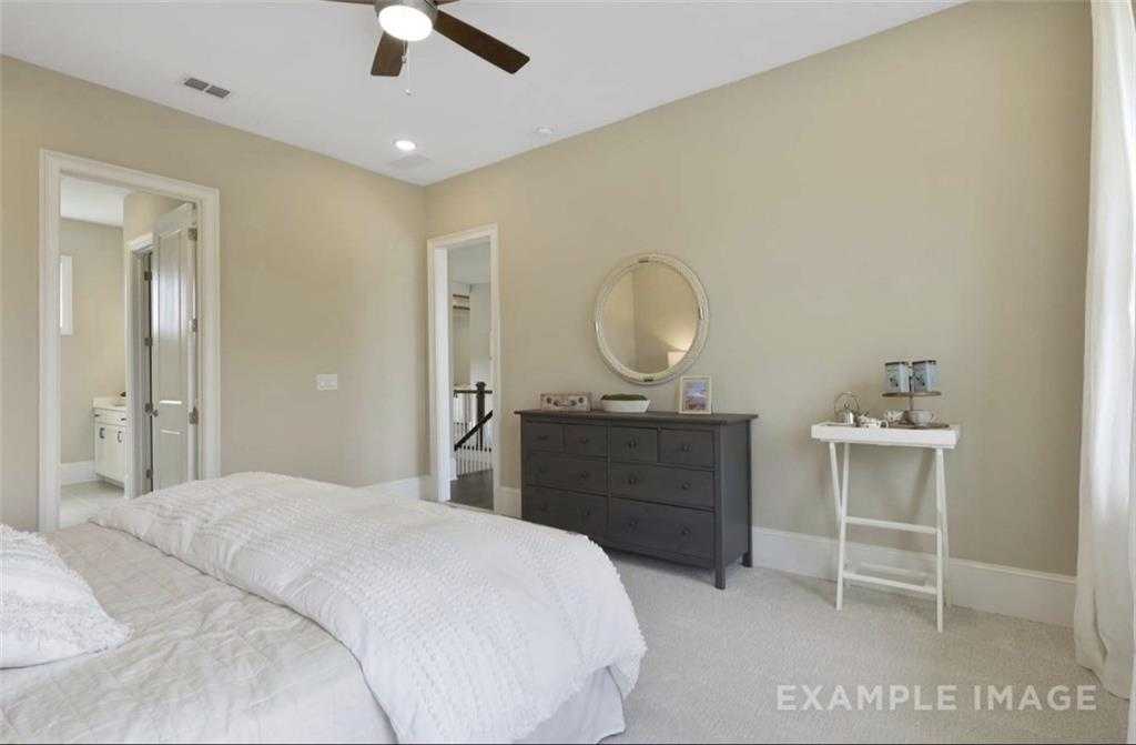 Elegant master bedroom with king bed, dark dresser, vanity mirror, and en-suite bath in Davidson Homes The Seaside A, Woodstock, GA