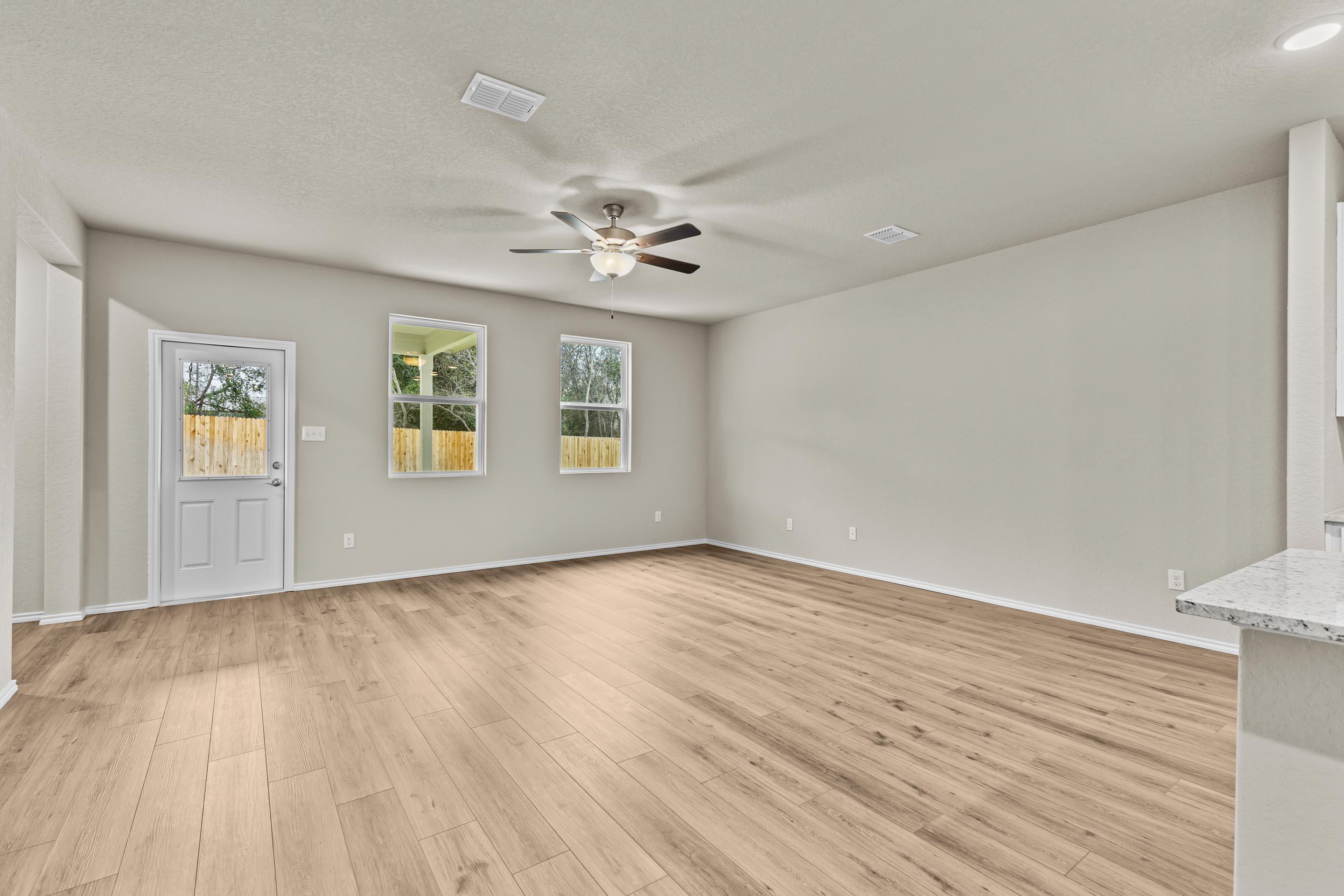 Spacious open living area with light hardwood floors, ceiling fan, large windows, and white quartz kitchen in Davidson Homes The Douglas F, San Antonio