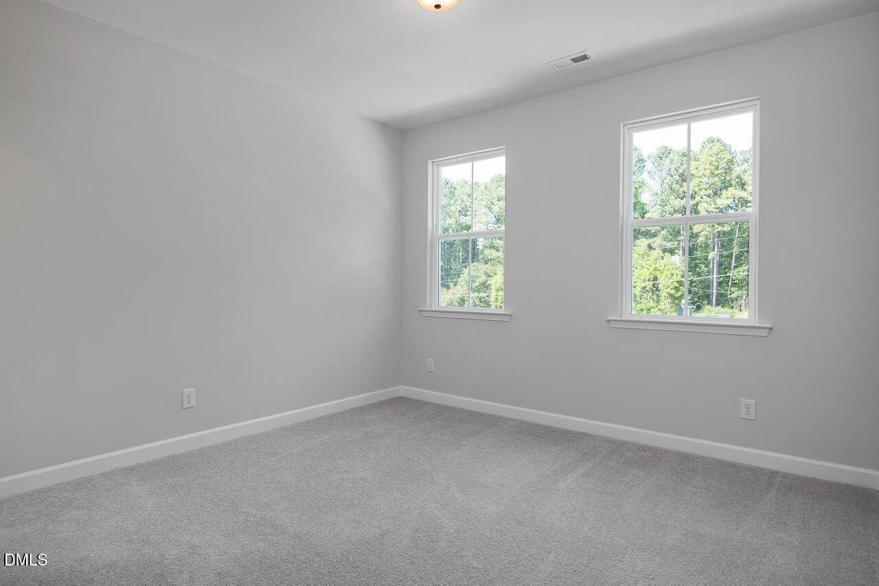 Bright, carpeted bedroom with neutral walls and windows in The Ashport L floor plan at Sage on North Main, Wake Forest.