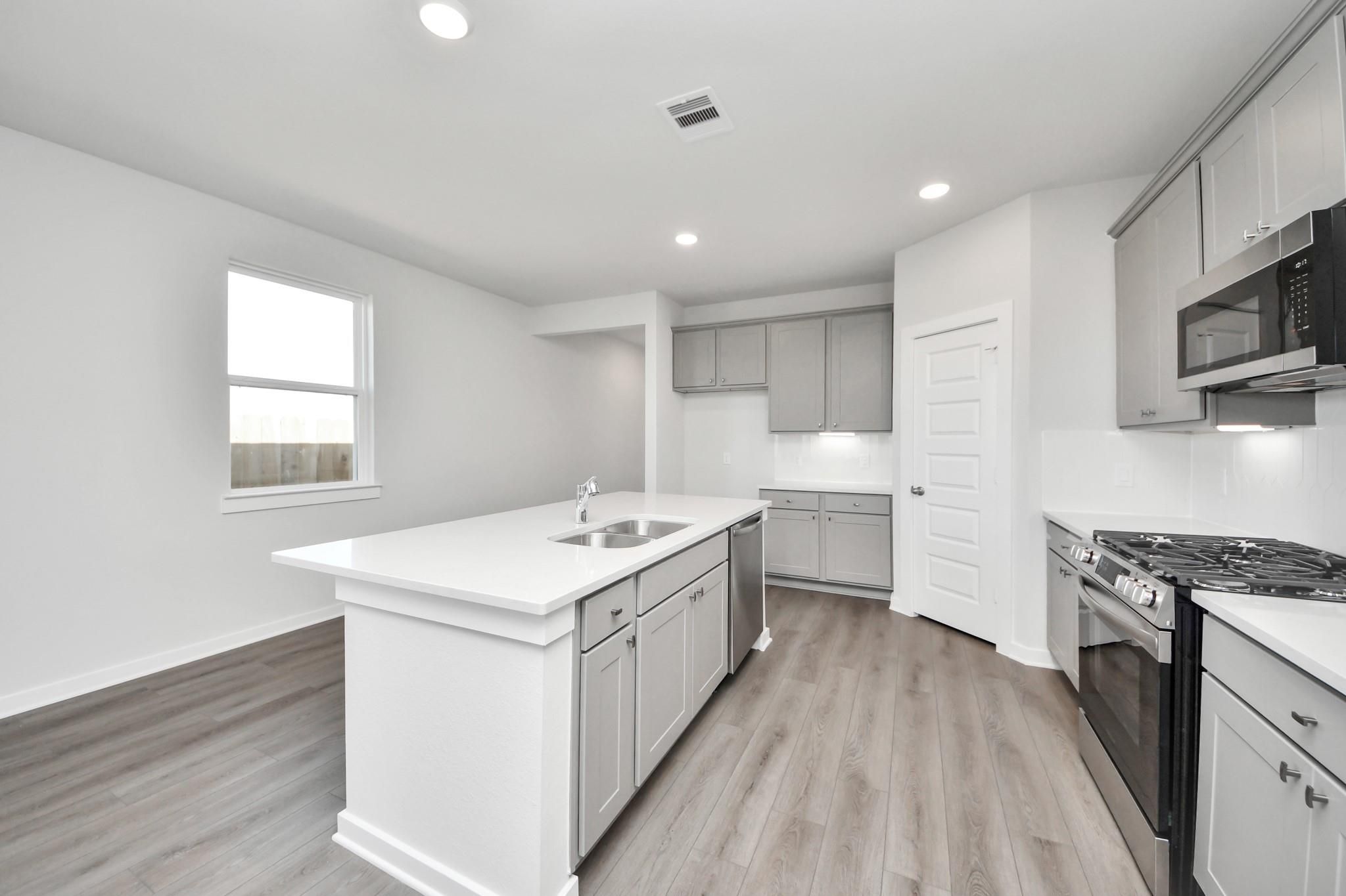 Modern kitchen with white quartz island and gray cabinets in The Riviera A floor plan at Emberly in Beasley, Texas.