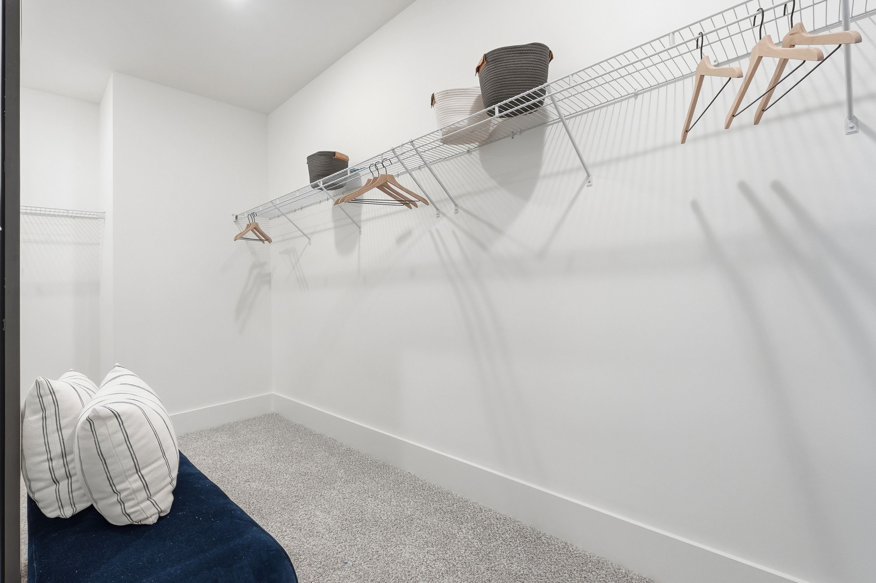 Spacious walk-in closet at Noble Ridge in Cullman Alabama with wire shelving, wooden hangers, gray carpet, and built-in bench
