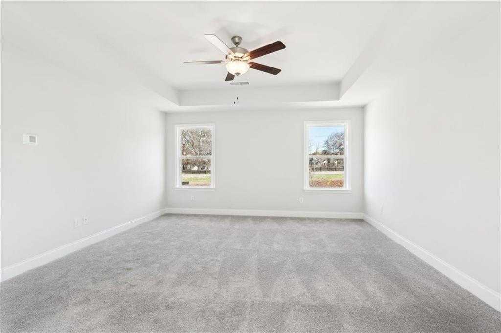 Bright secondary bedroom with tray ceiling, ceiling fan, large windows, and gray carpet in The Hickory C, Hoschton, Georgia