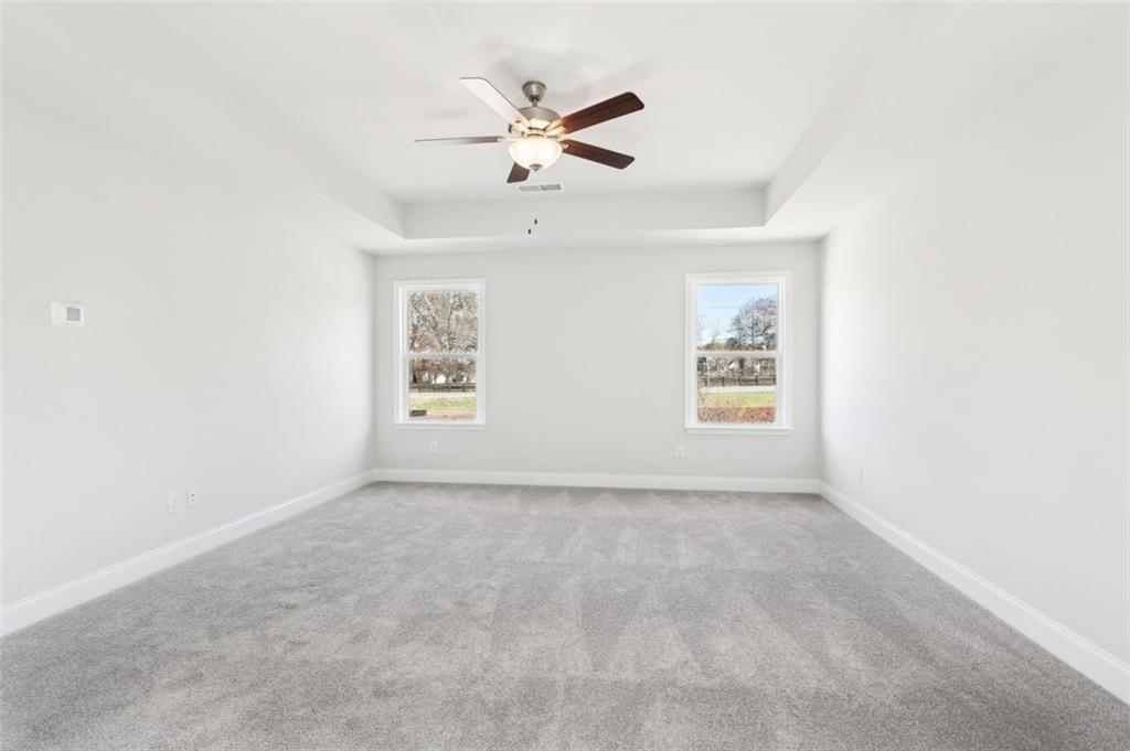 Bright secondary bedroom with tray ceiling, ceiling fan, large windows, and gray carpet in The Hickory C, Hoschton, Georgia