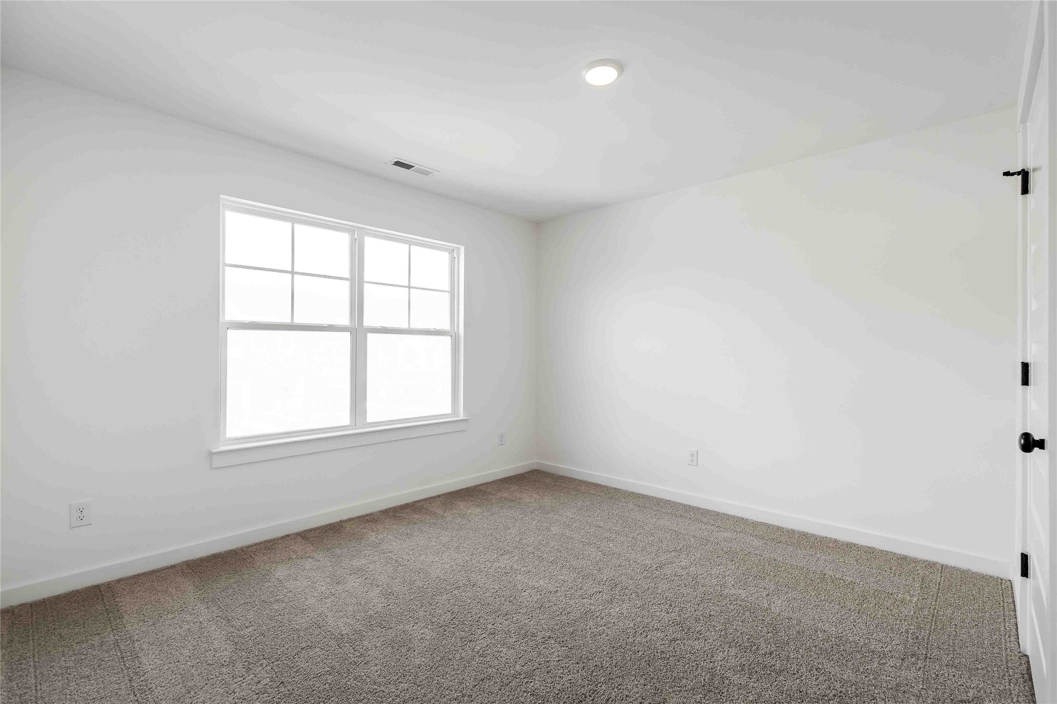 Bright, carpeted secondary bedroom with white walls in The Ash O floor plan by Davidson Homes in Heartland, Texas.