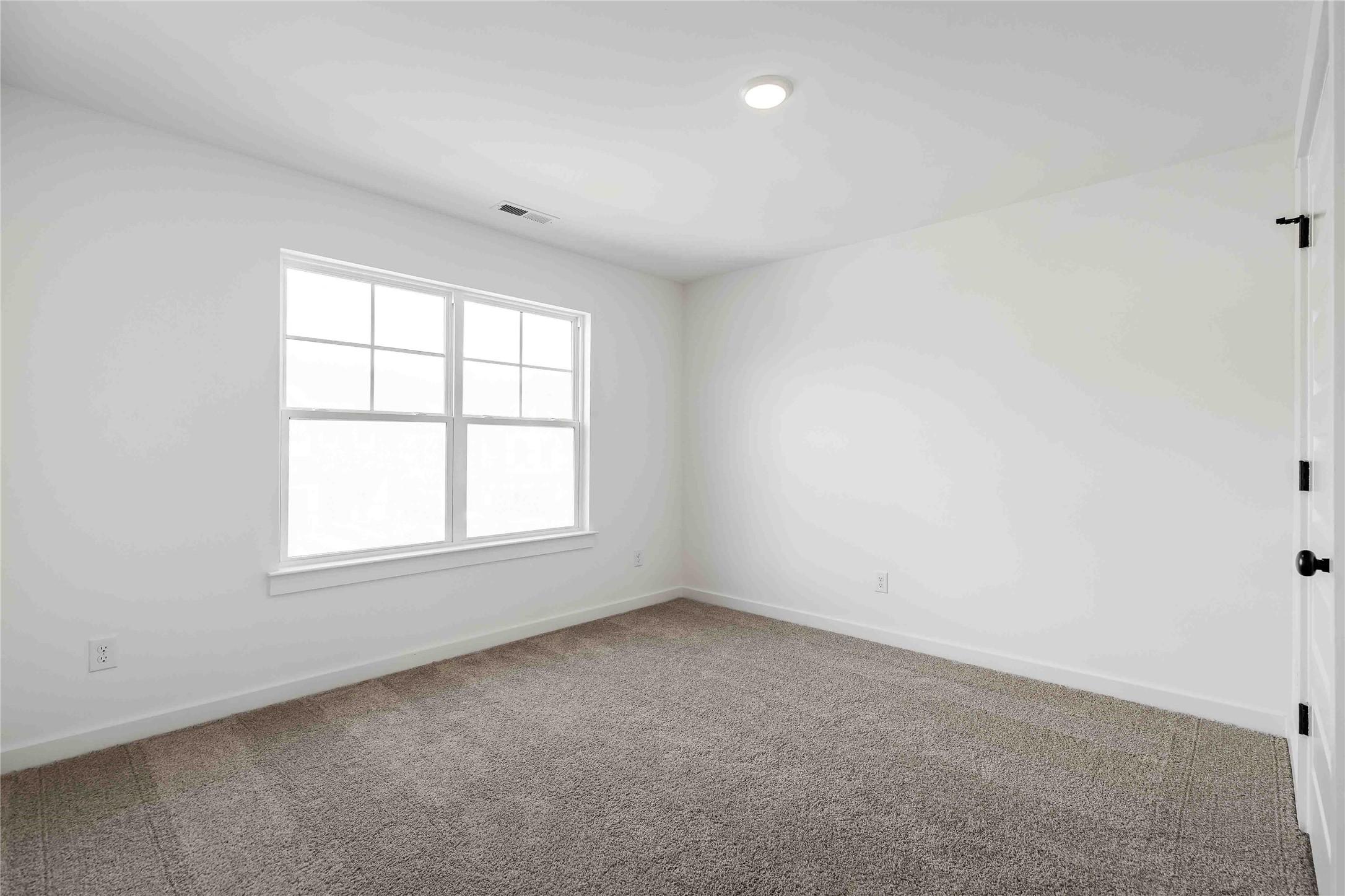 Bright, carpeted secondary bedroom with white walls in The Ash O floor plan by Davidson Homes in Heartland, Texas.