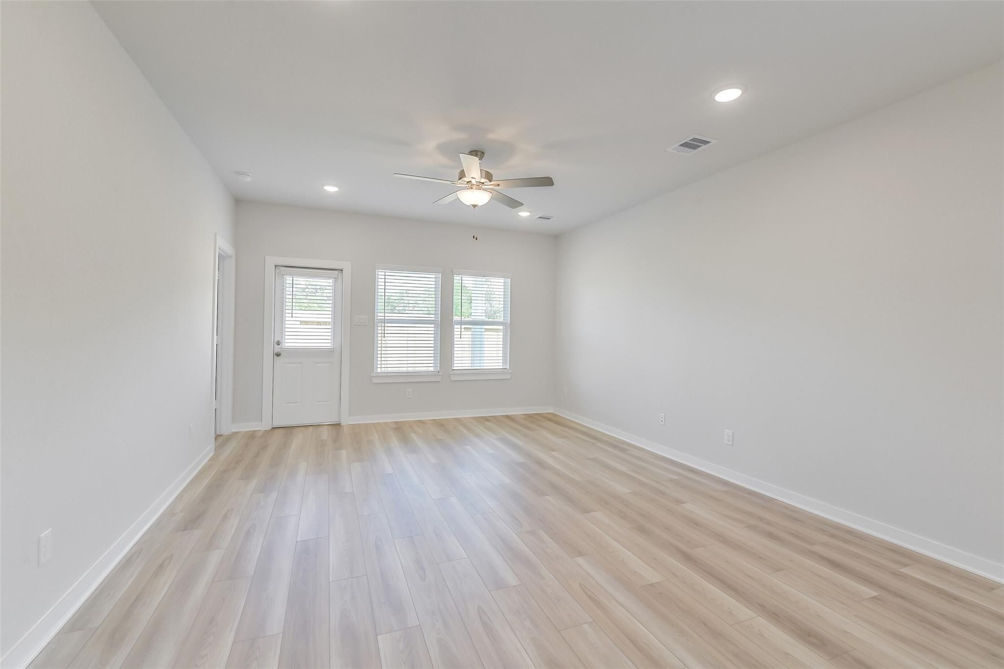 Spacious living room with light oak laminate floors, ceiling fan, recessed lights, and large windowed walls in Davidson Homes San Marcos E, Conroe, Texas