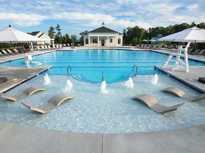 Resort-style community pool at Addison West in Holly Springs NC with lounge chairs, umbrellas, water fountains, and pavilion backdrop