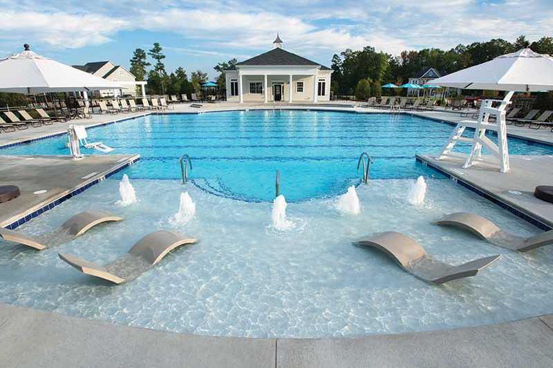 Resort-style community pool at Addison West in Holly Springs NC with lounge chairs, umbrellas, water fountains, and pavilion backdrop