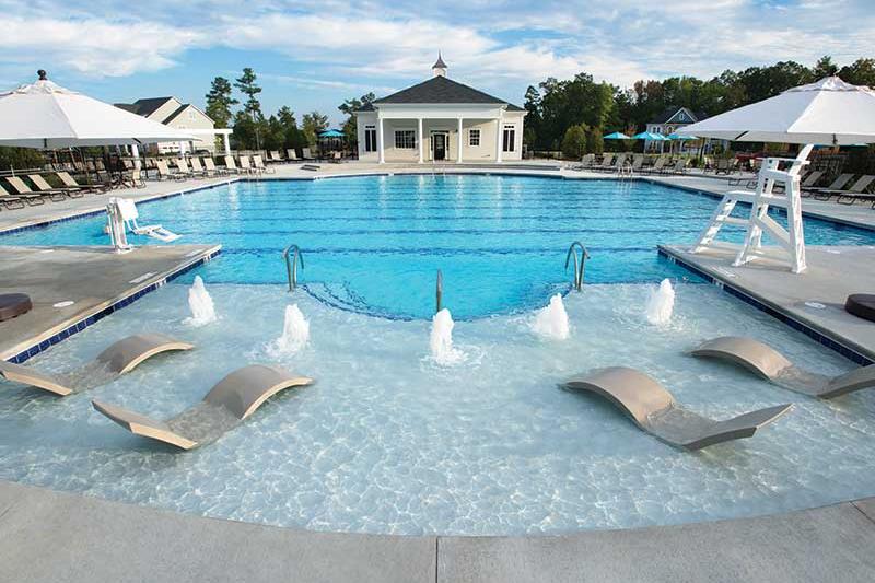 Resort-style community pool at Addison West in Holly Springs NC with lounge chairs, umbrellas, water fountains, and pavilion backdrop
