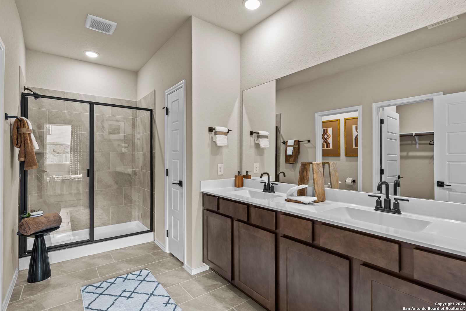 Modern master bathroom with double vanity, glass walk-in shower, and wood cabinets in Davidson Homes The Douglas F, San Antonio