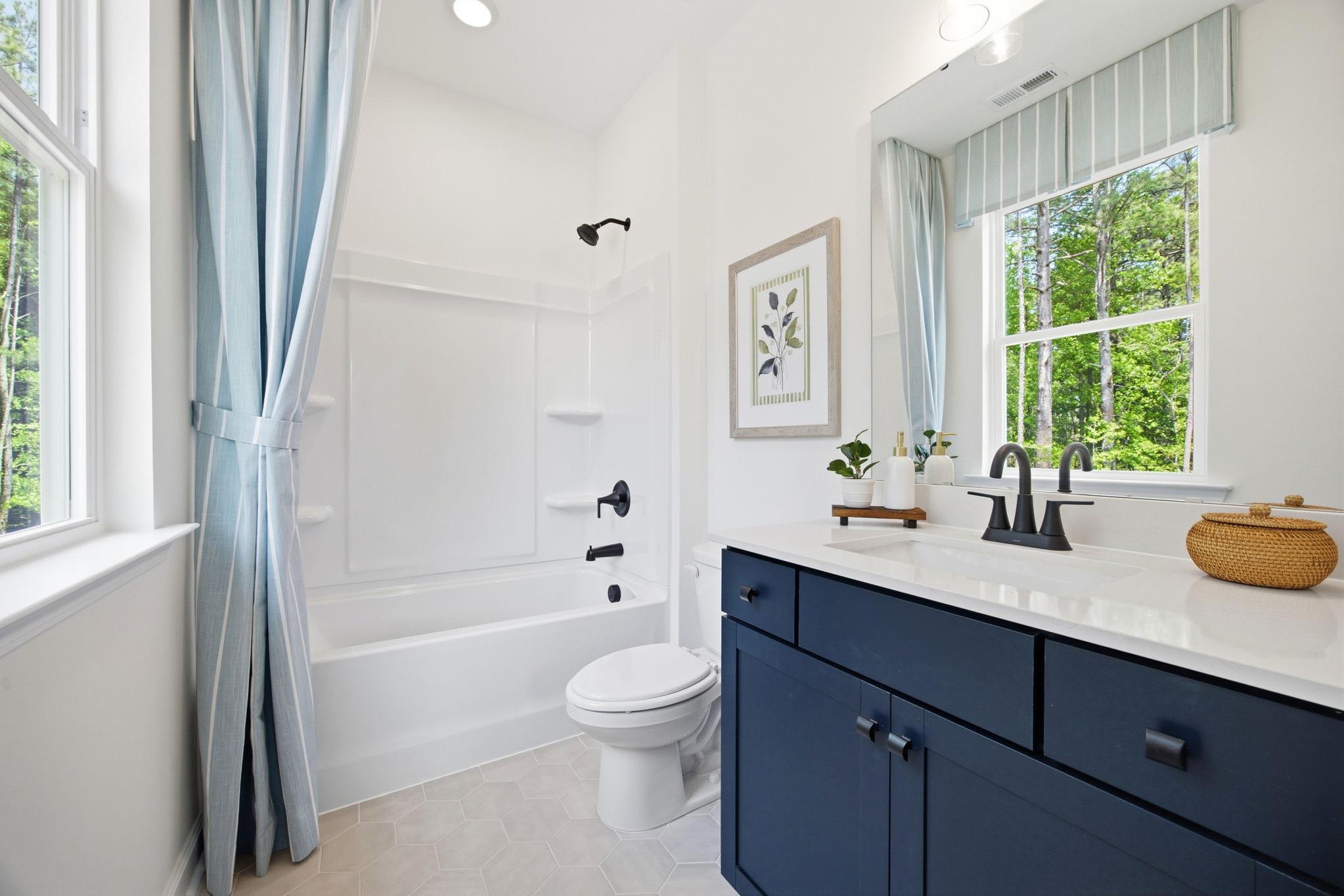 Bright bathroom in The Ashport K featuring a navy blue vanity, white tub-shower combo, and light blue striped curtains.