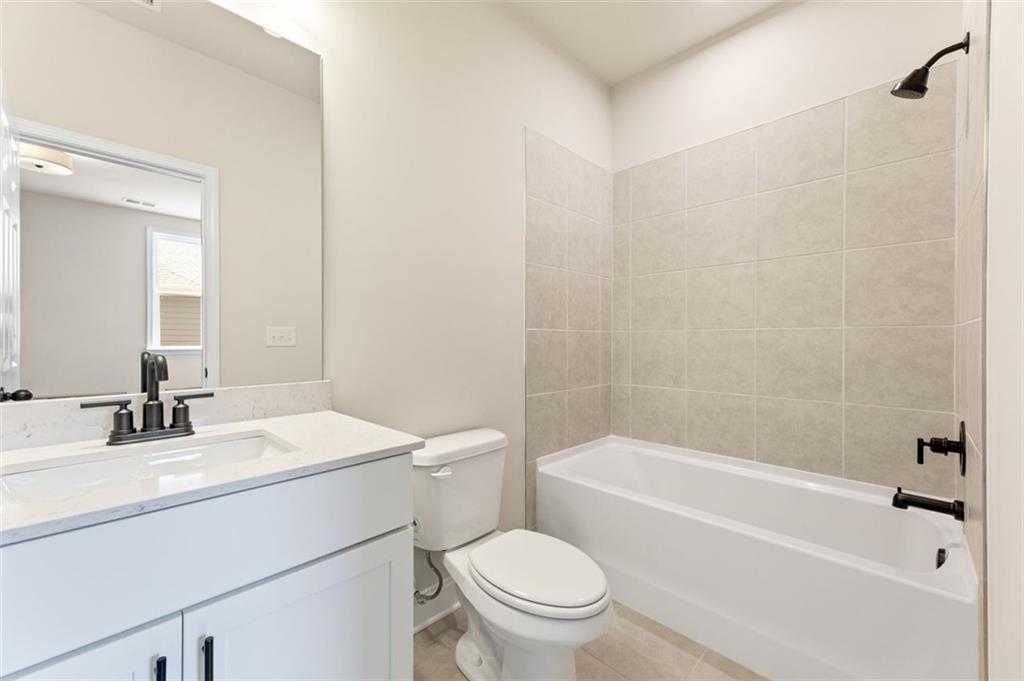 Modern bathroom with white vanity, bathtub-shower combo, and neutral tile walls in Davidson Homes The Harrison G, Hoschton, GA