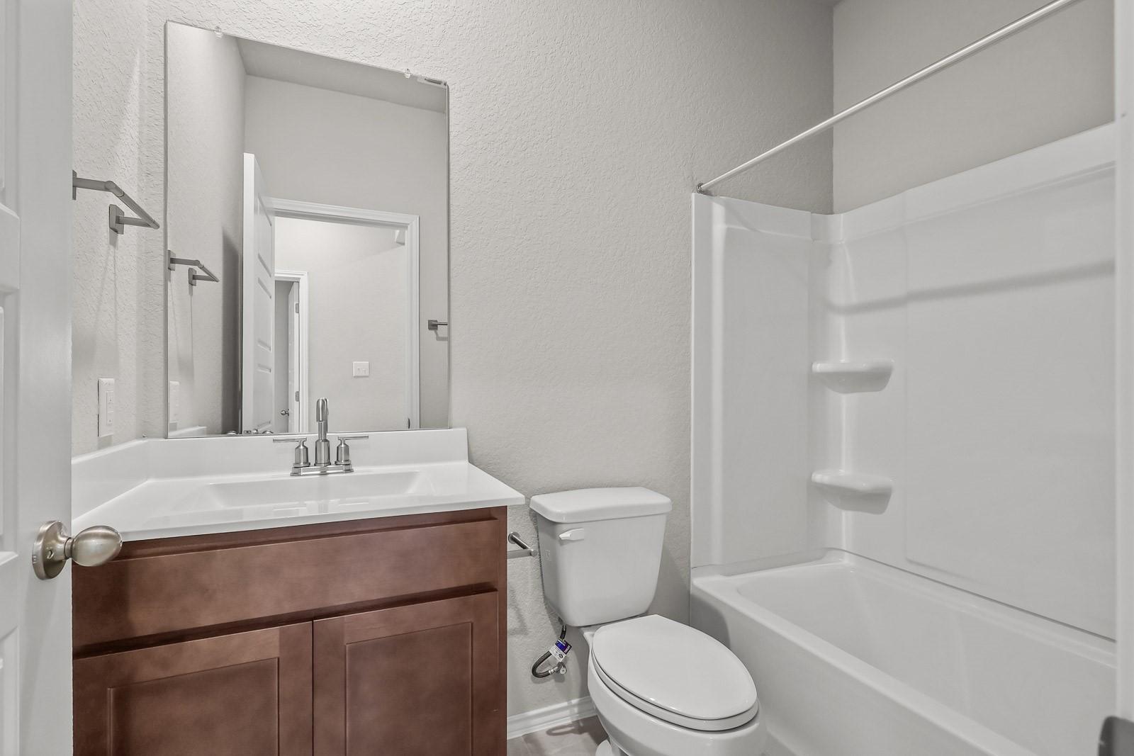 Modern guest bathroom with wood vanity and tub-shower combo in The Frio G floor plan by Davidson Homes in Heartland, Texas.