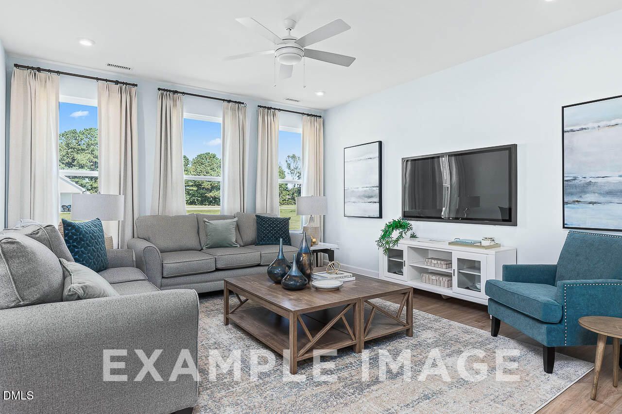 Bright living room with gray sofas, blue accent chair, and large windows in Davidson Homes The Ash C, Lillington, North Carolina