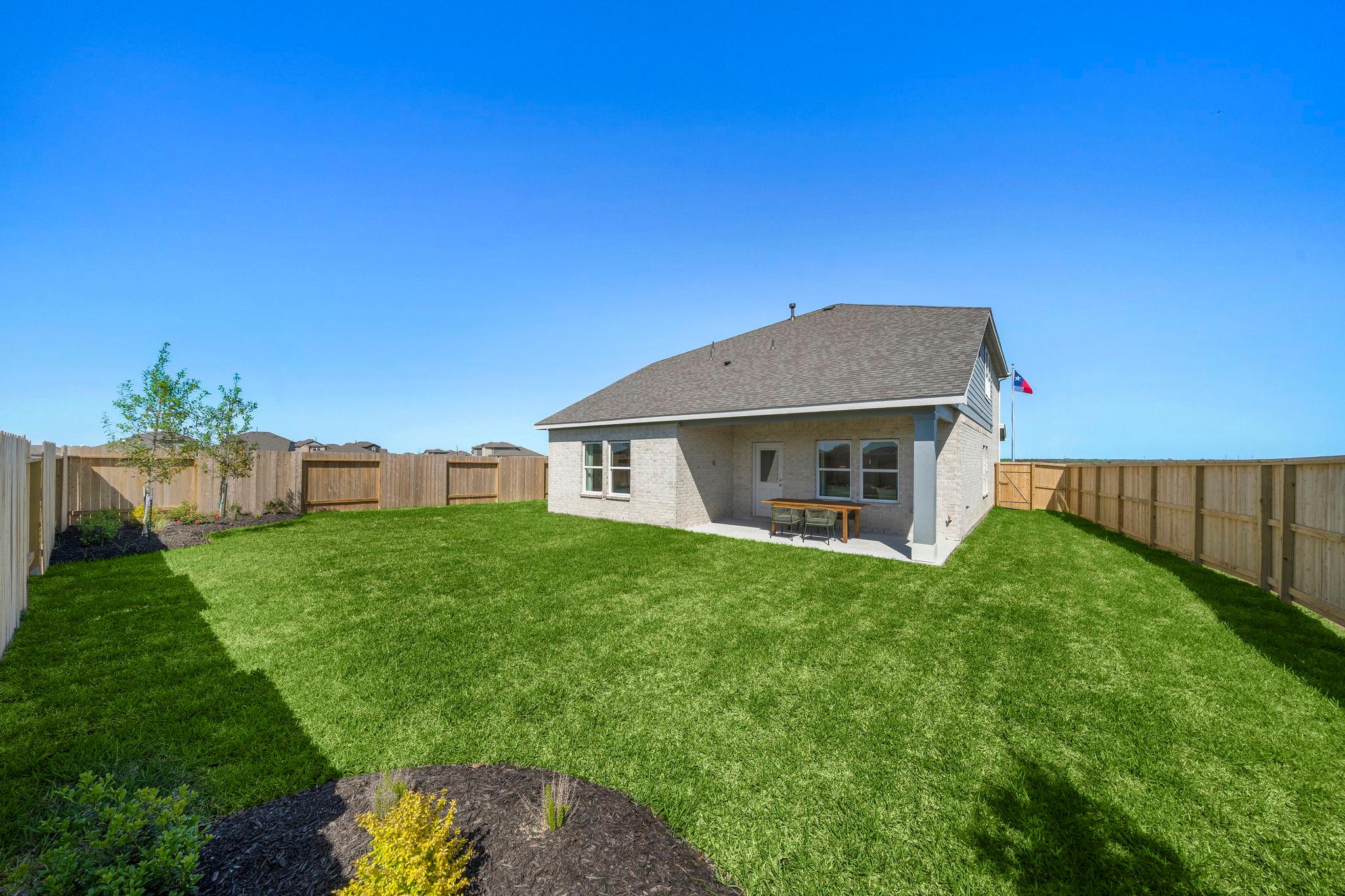 Spacious backyard patio with picnic table and lush green lawn at River Ranch Meadows in Dayton, Texas by Davidson Homes