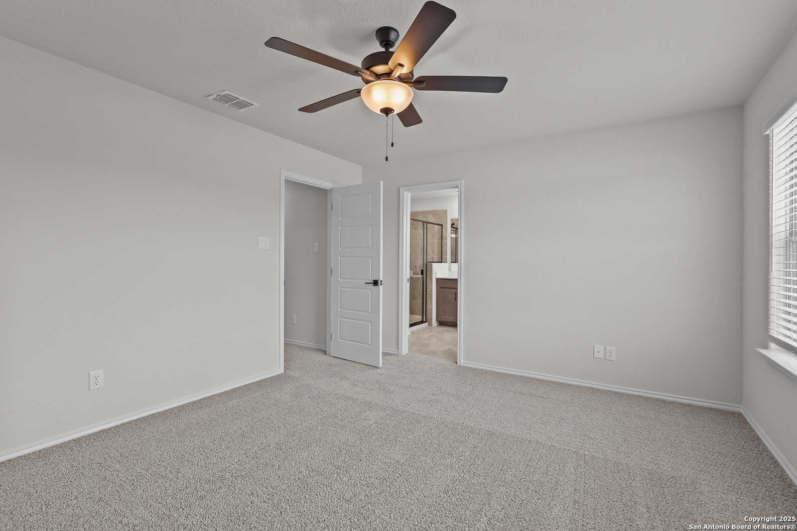 Bright secondary bedroom with ceiling fan, carpet floors, and attached bath in Davidson Homes The Florence C, San Antonio