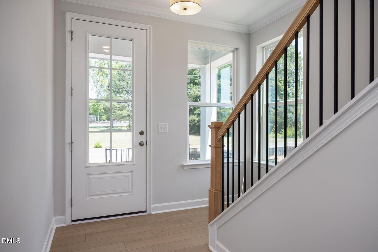 Bright entryway with glass-paneled door and wood staircase in The Mitchell floor plan by Davidson Homes in Knightdale, NC.