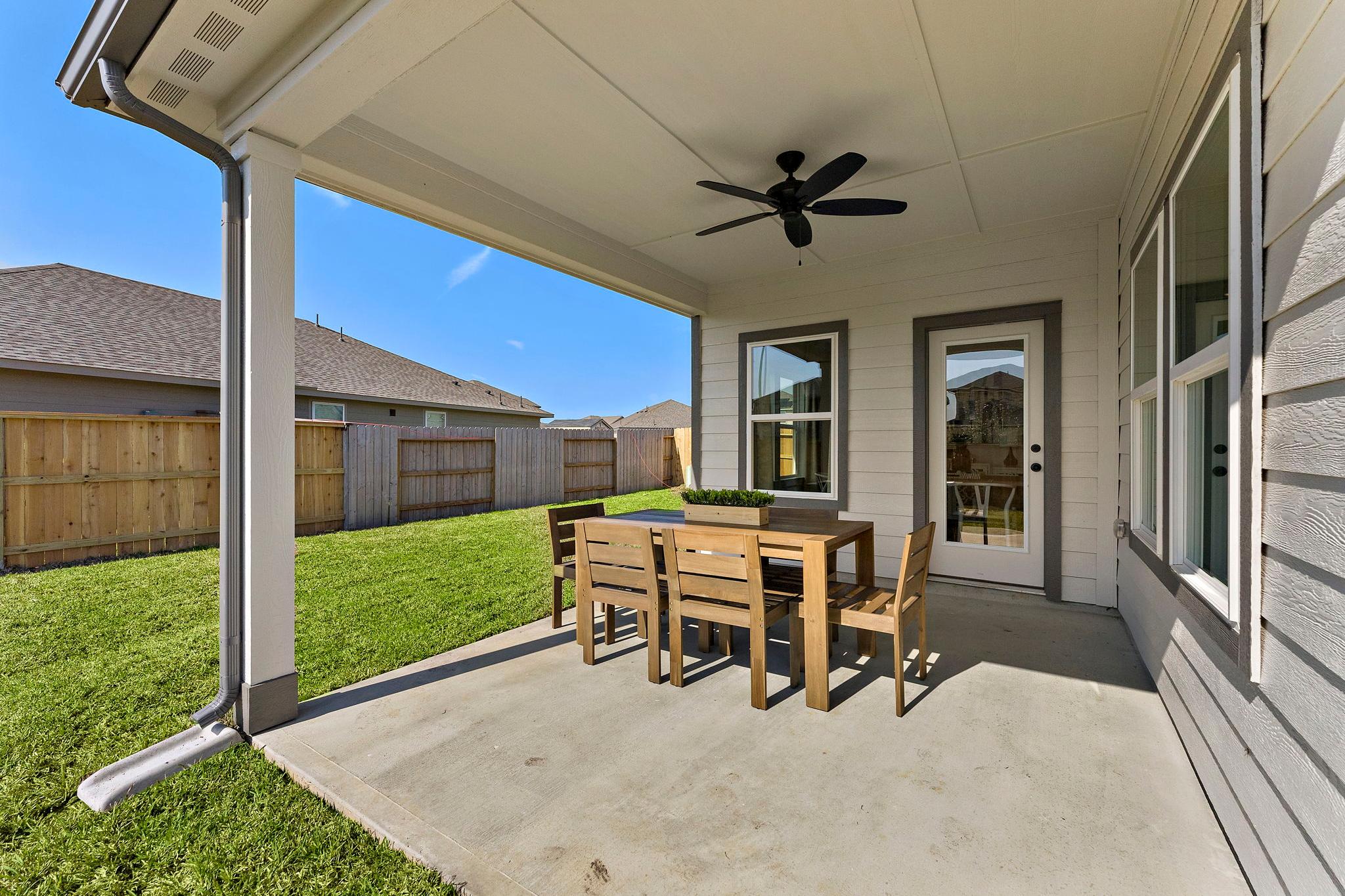 Covered patio at Sundance Cove in Crosby Texas with wooden dining table chairs ceiling fan and lush green backyard