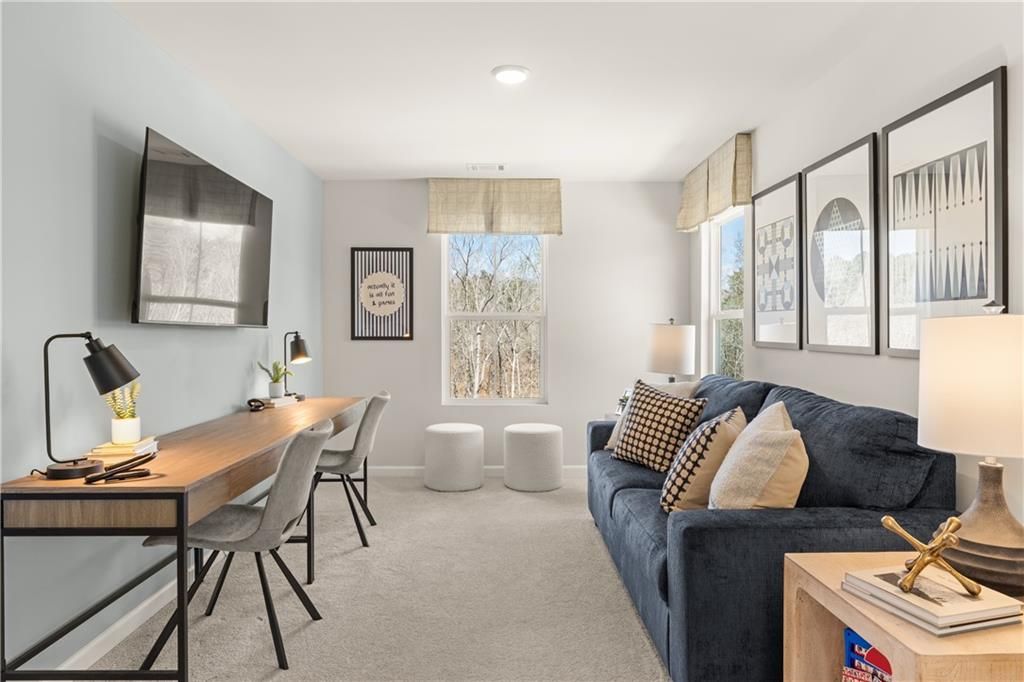 Cozy upstairs loft with wooden desk, blue sofa, wall-mounted TV, and window view in Davidson Homes The Burton C, Canton, GA