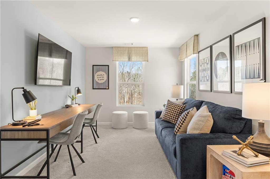 Cozy upstairs loft with wooden desk, blue sofa, wall-mounted TV, and window view in Davidson Homes The Burton C, Canton, GA