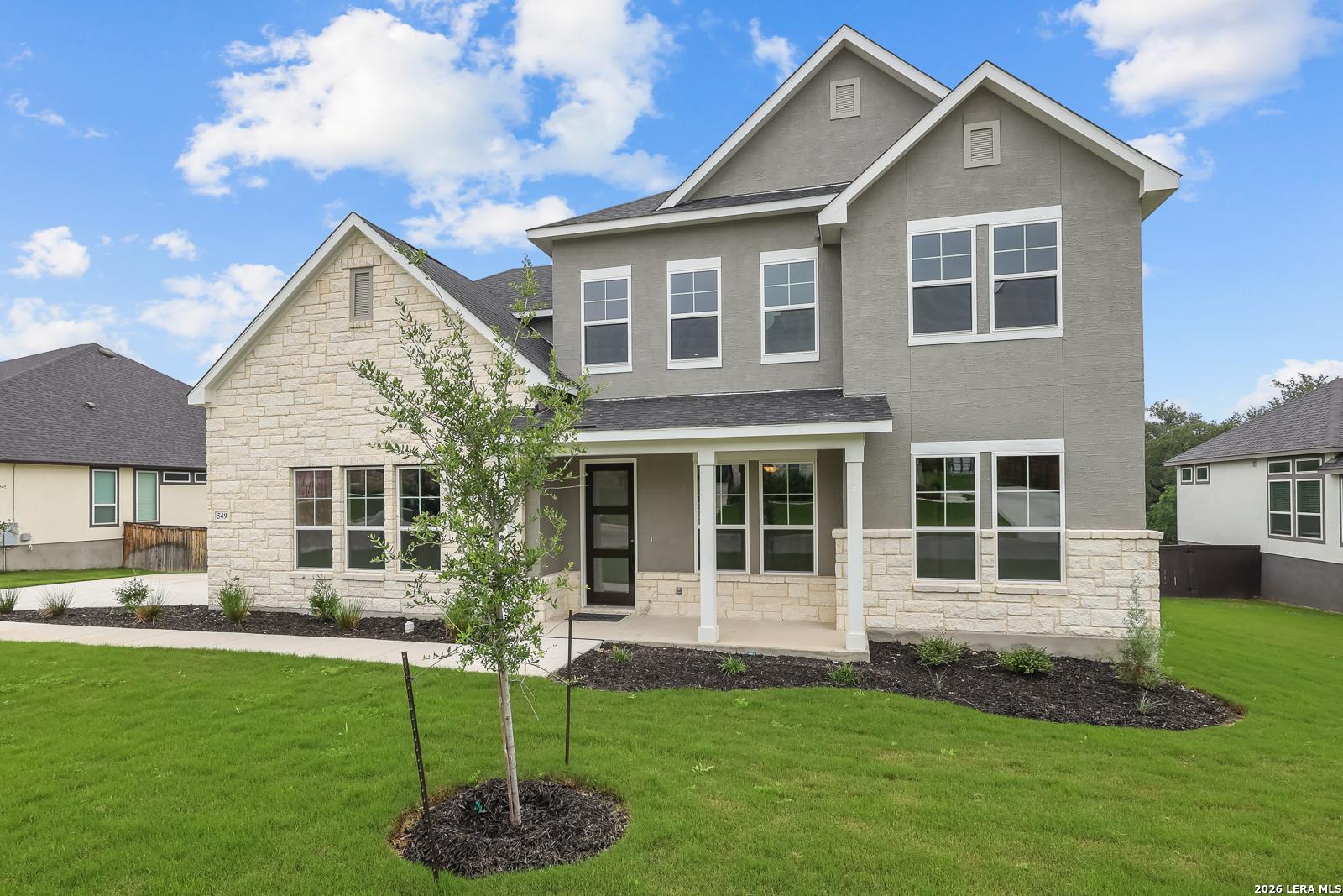 Modern 2-story Belmont H home by Davidson Homes: gray stone facade, covered porch, large windows, lush green yard in Potranco Oaks, Castroville TX