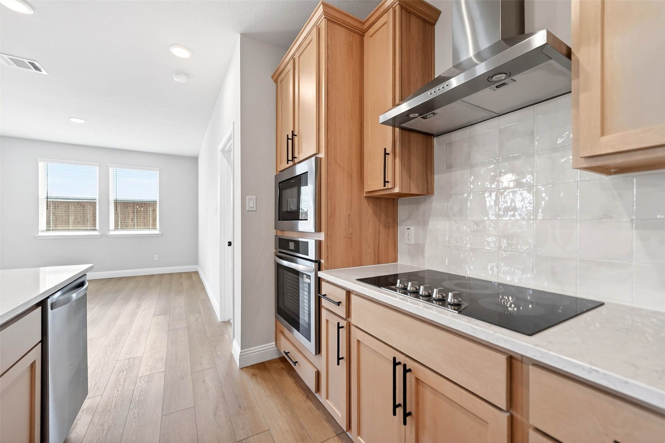 Modern kitchen with natural wood cabinets, stainless steel appliances, and tile backsplash in The Holly C plan, Anna, TX.