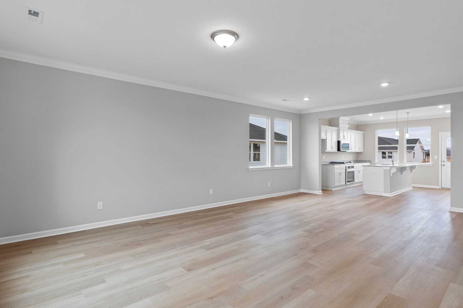 Spacious open-concept kitchen and living area in The Stella home design with gray walls, light wood floors, white cabinets