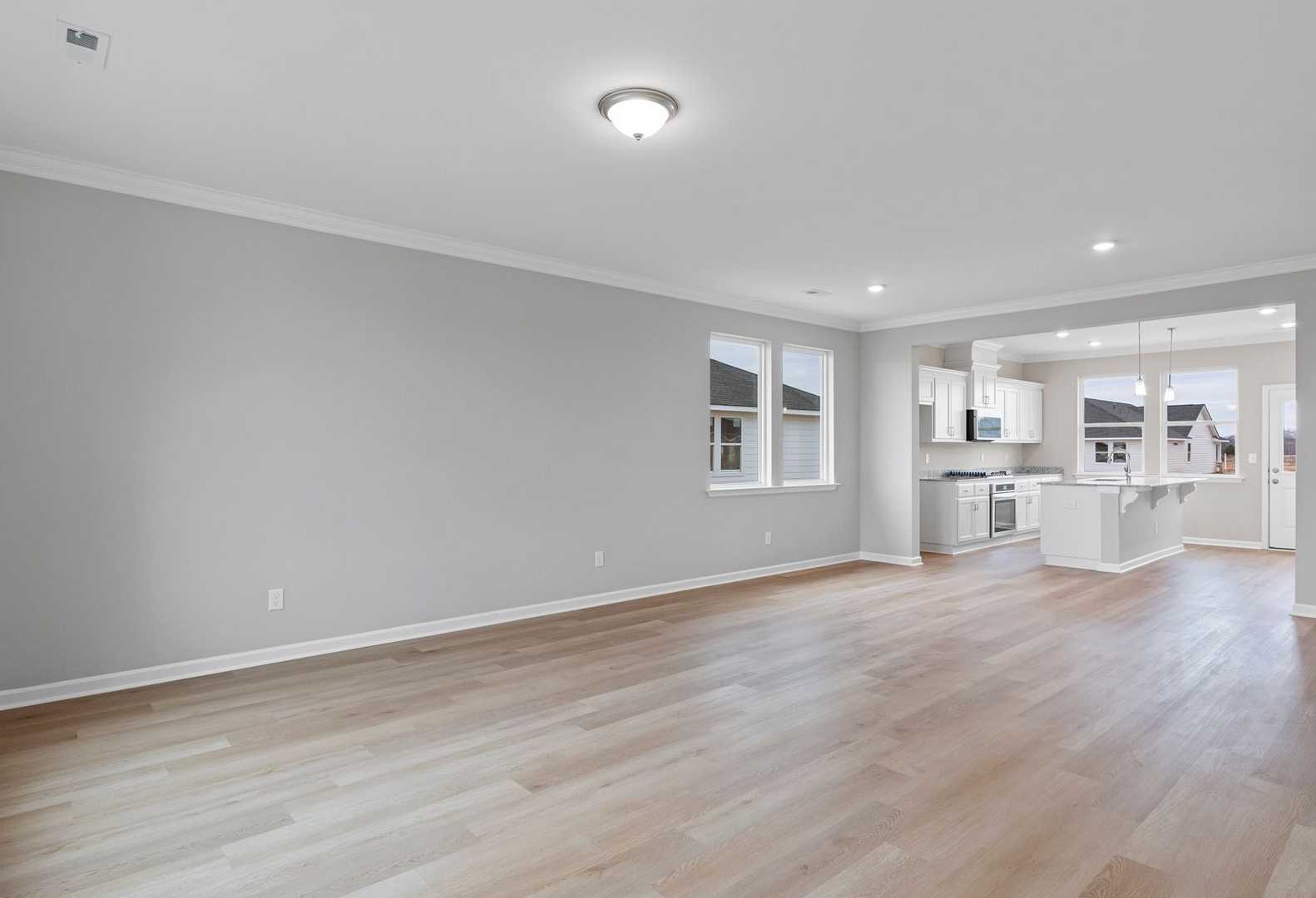 Open-concept living and kitchen in The Stella A home with light wood floors, gray walls, white cabinets, and large windows