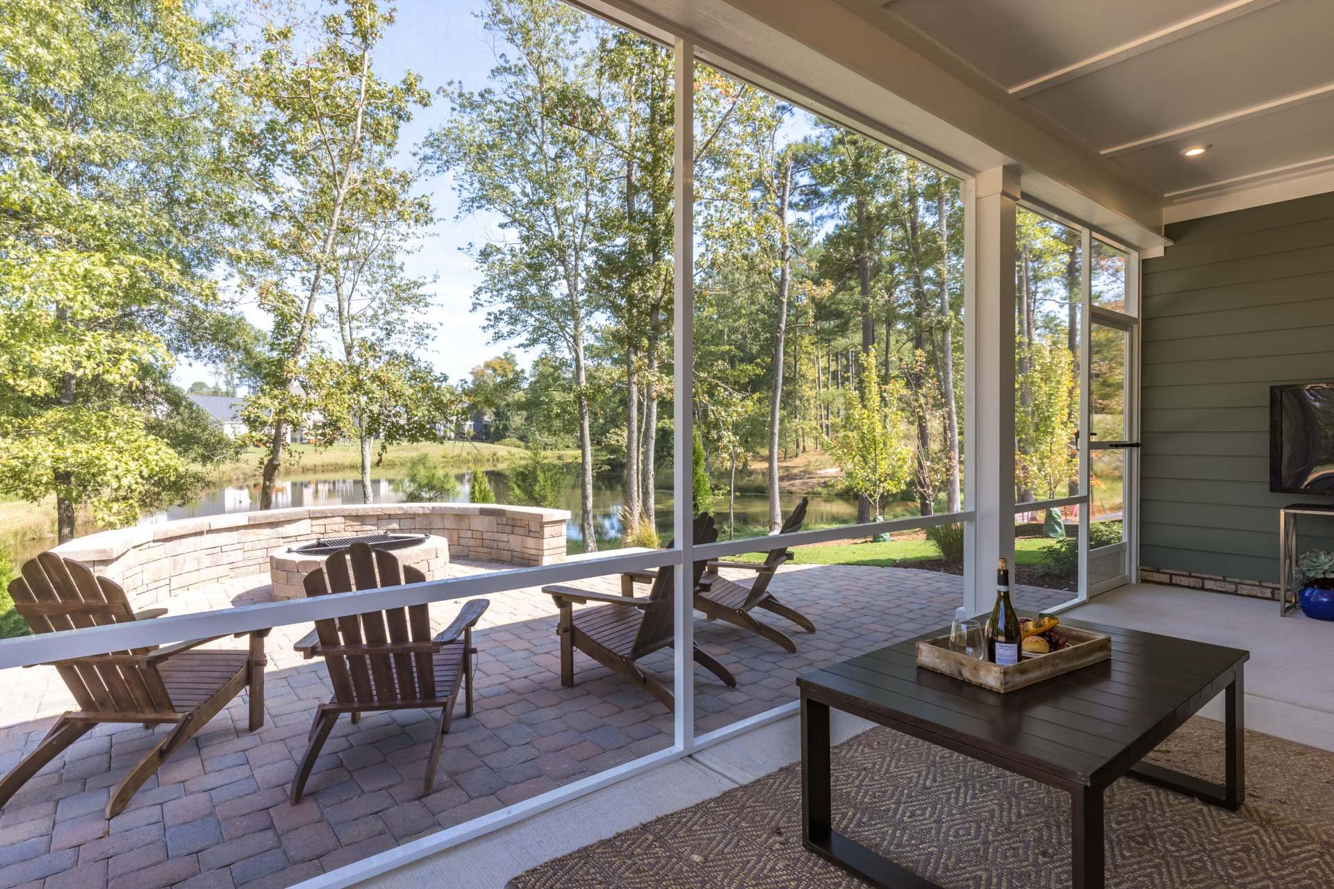 Screened porch at Glenmere in Knightdale NC by Davidson Homes with Adirondack chairs, coffee table, and wooded backyard view of fire pit and pond