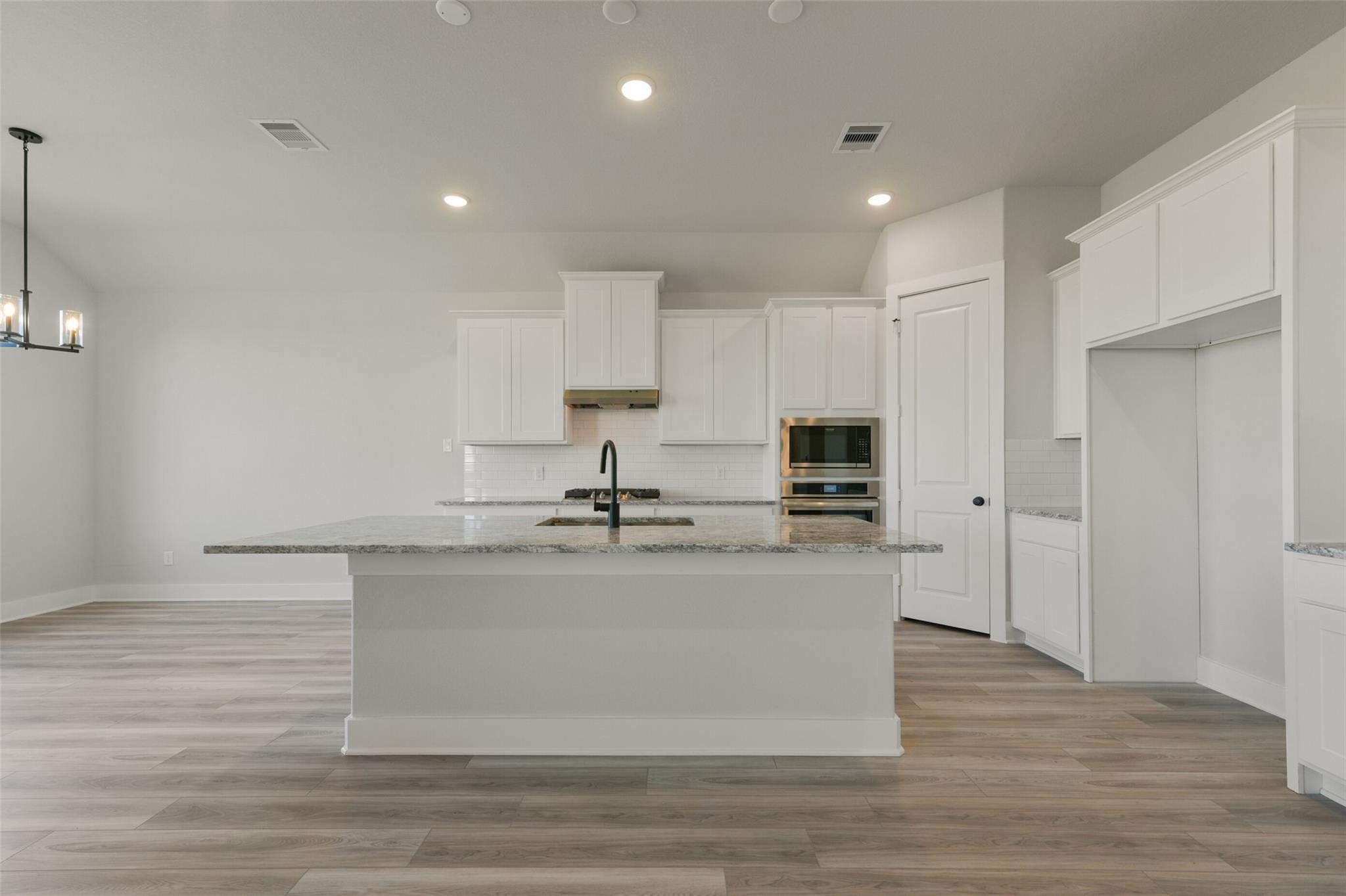 Modern white kitchen with granite island, stainless appliances, and open layout in Davidson Homes The Edward C, Lago Mar