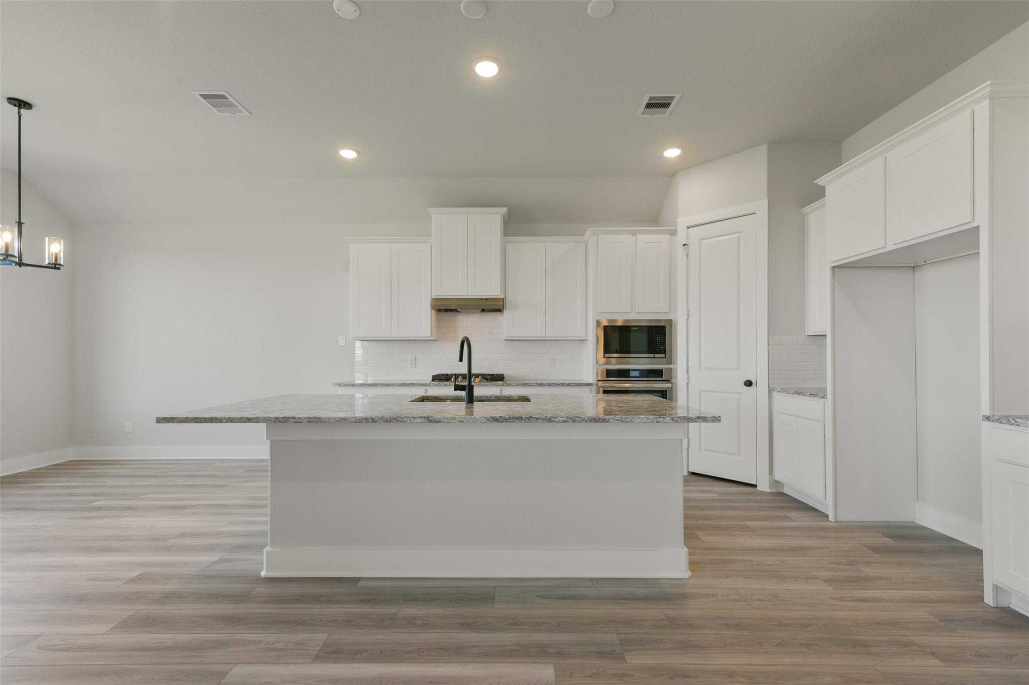 Modern white kitchen with granite island, stainless sink, oven, and open layout in Davidson Homes The Edward C, Lago Mar, Texas City