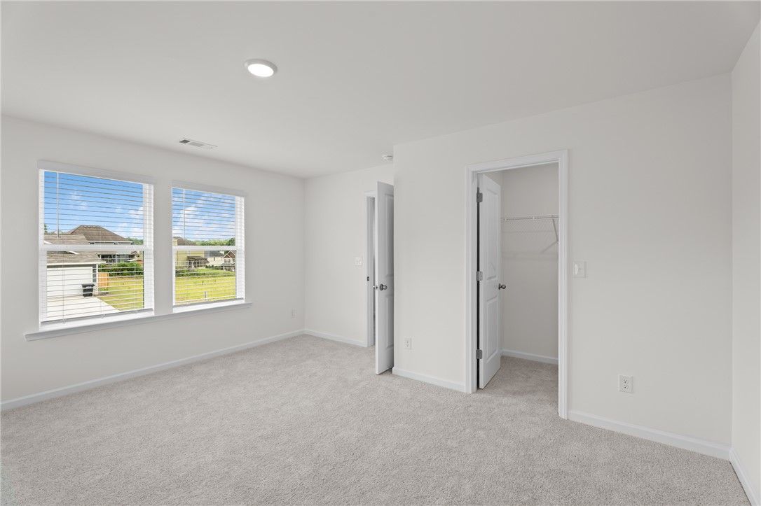 Bright bedroom with neutral carpet and walk-in closet in The Stella D floor plan at Silver Oak, Cusseta, Alabama.