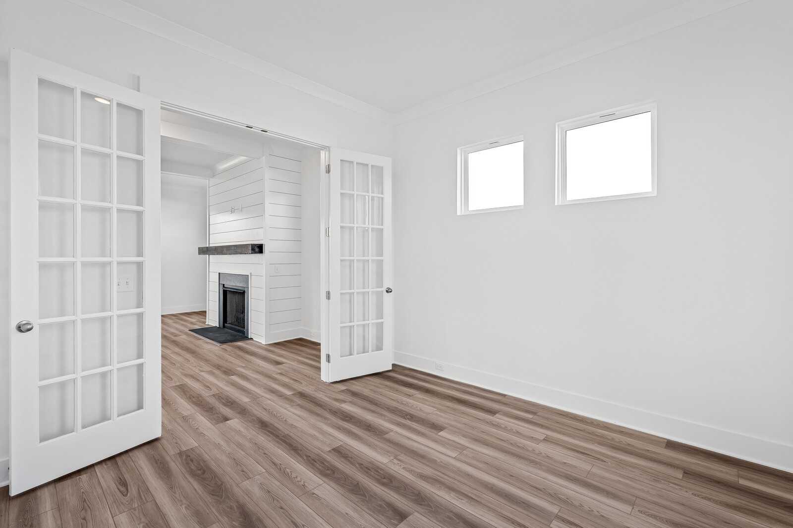 Bright living room with open French doors to white brick fireplace and wood floors in The Alston A home, Murfreesboro, TN