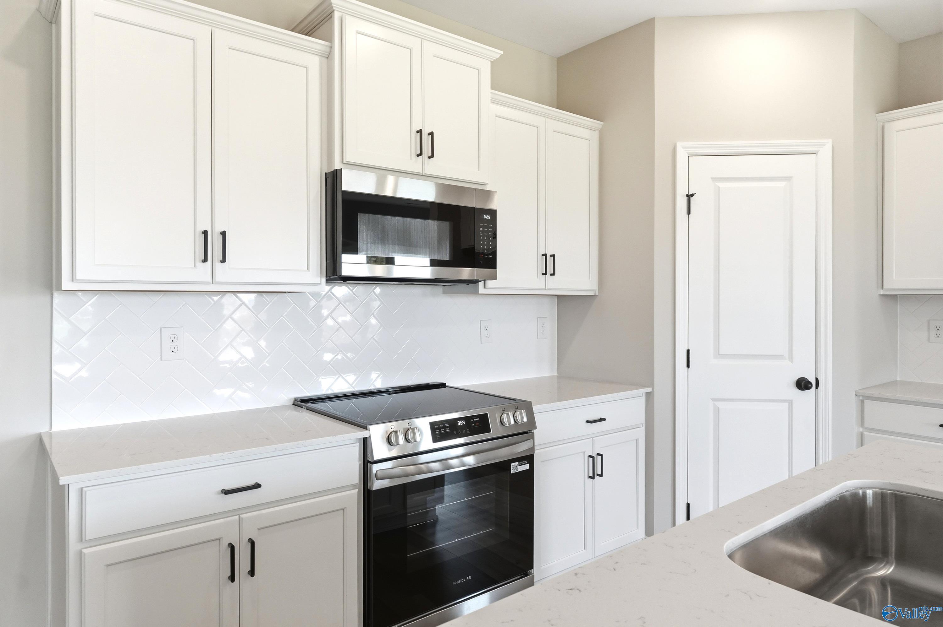 Modern kitchen with white cabinets, herringbone backsplash, and stainless appliances in The Daphne D, Creekside, Harvest.