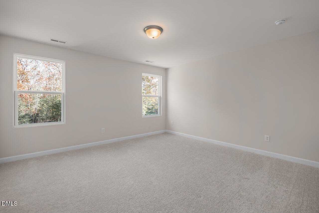 Bright secondary bedroom with neutral walls, beige carpet, and large windows showing fall foliage in The Gavin C, Lillington, NC