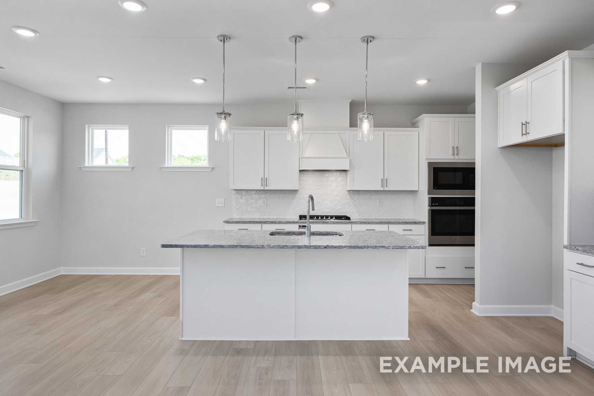 Spacious modern kitchen in The Gavin C with white cabinetry, granite island, double ovens, and pendant lights