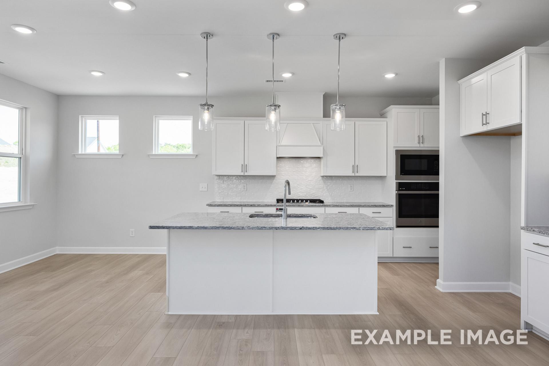 Modern kitchen in The Gavin B by Davidson Homes: white cabinets, large island with sink, stainless ovens, pendant lights, open layout