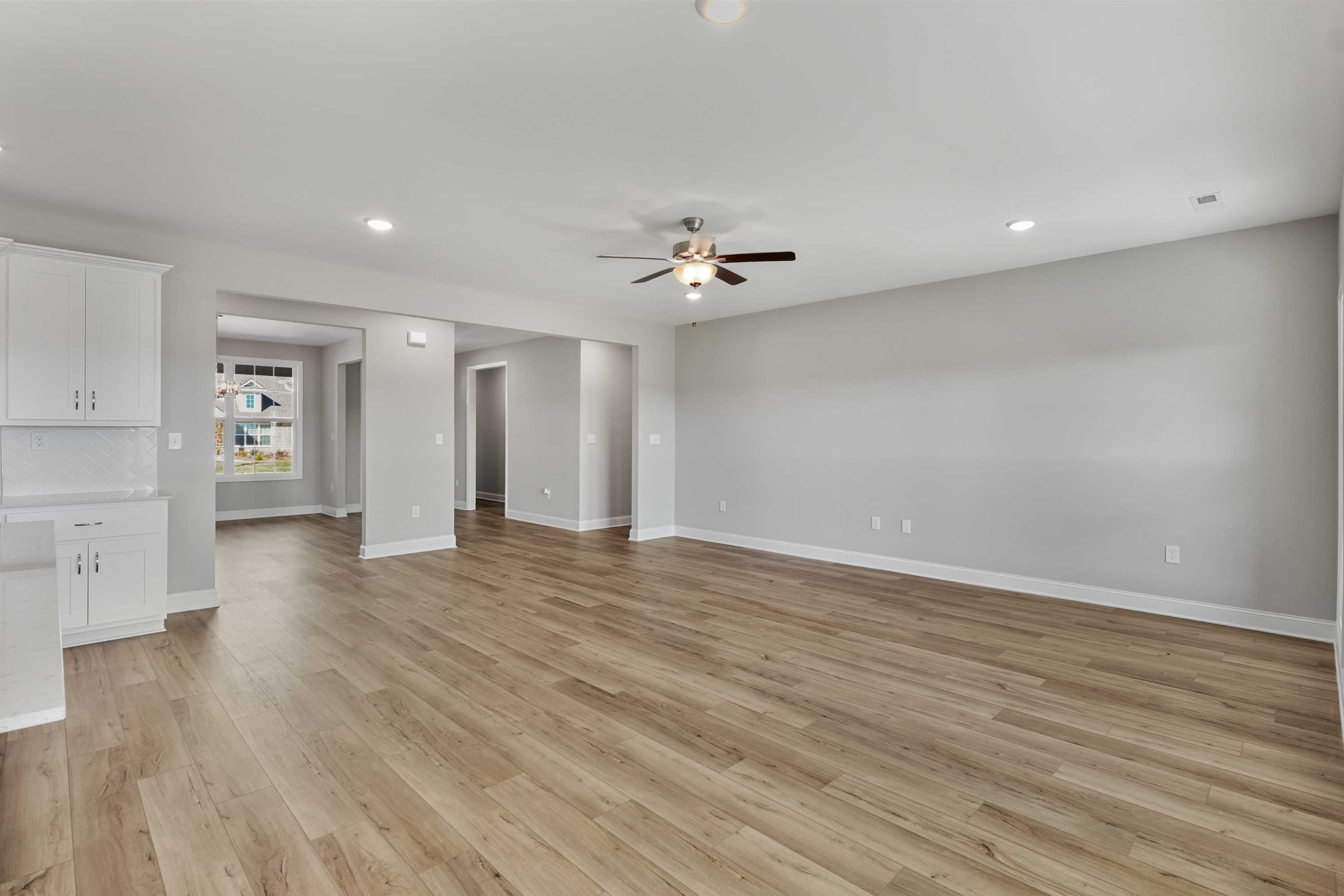 Open-concept kitchen and great room in The Valencia home with white cabinets, hardwood floors, gray walls, and ceiling fans