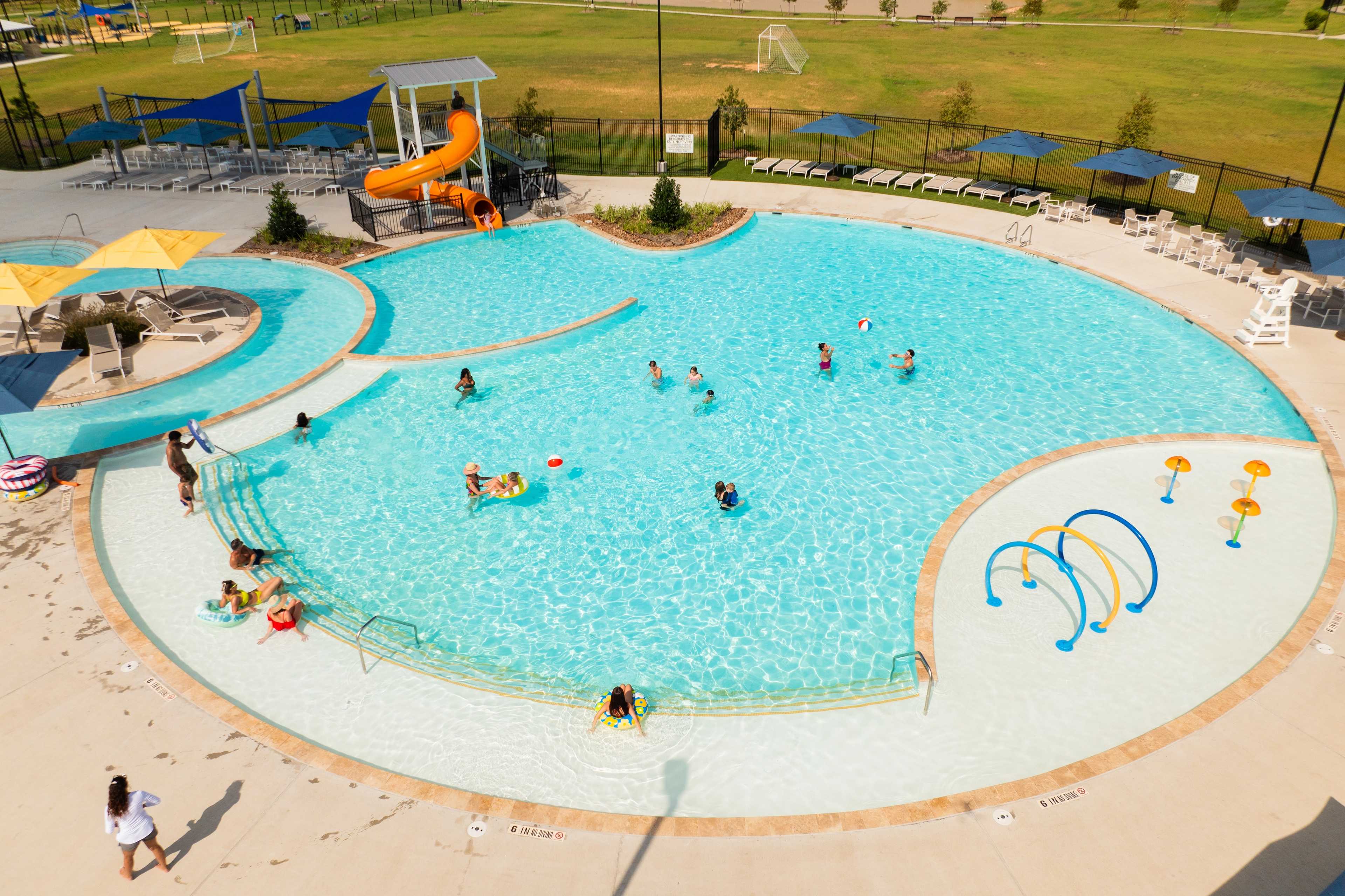 Resort-style pool and splash pad at Sunterra in Katy Texas with kids swimming orange slide and lounge chairs