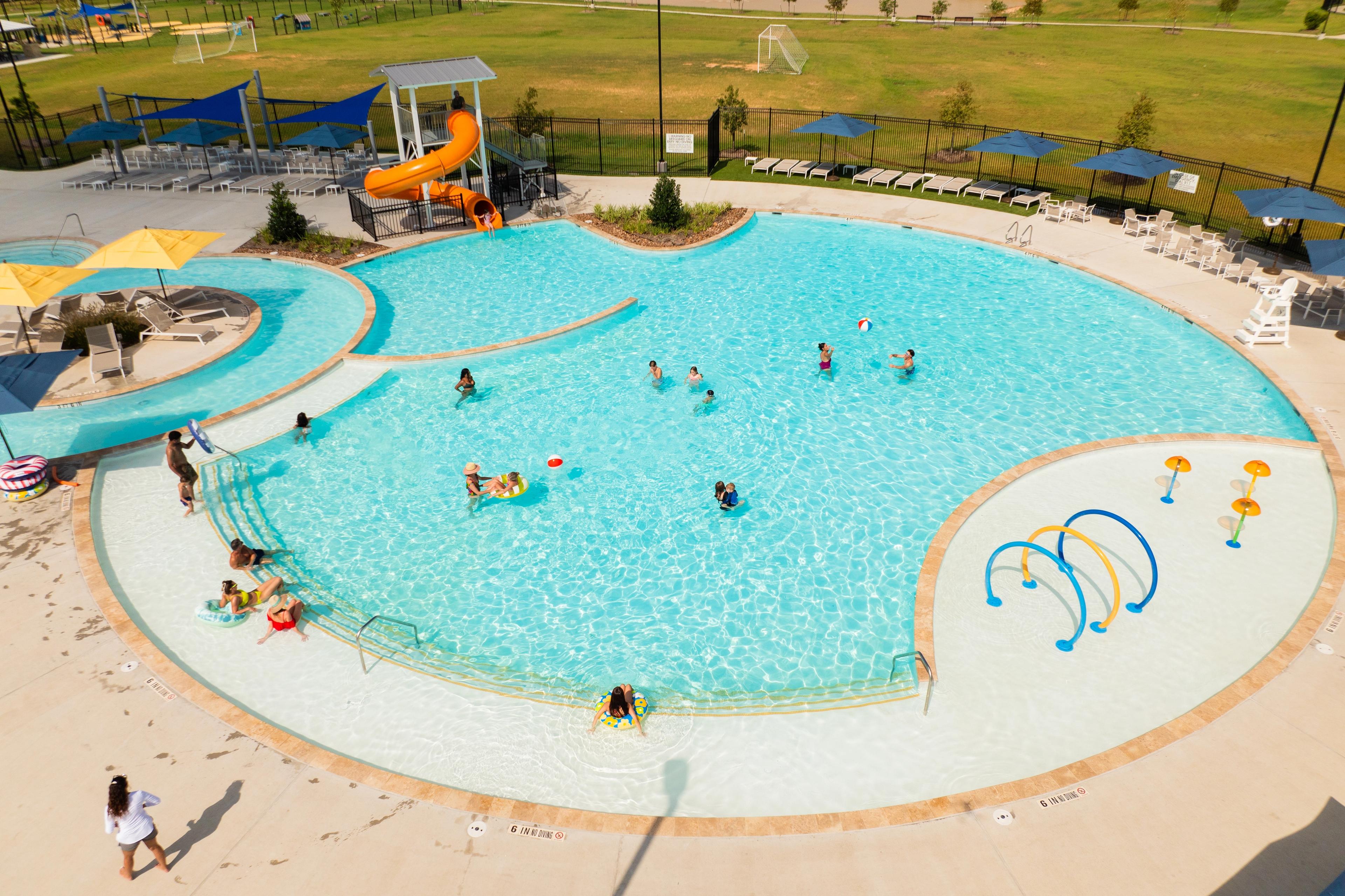 Resort-style pool and splash pad at Sunterra in Katy Texas with kids swimming orange slide and lounge chairs