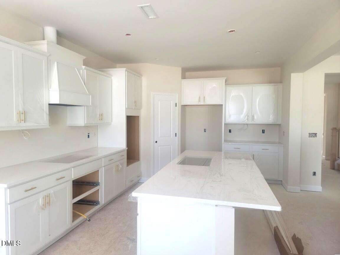 Modern white shaker kitchen with quartz island, hood vent, and open layout in Davidson Homes The Cypress B II, Angier, NC