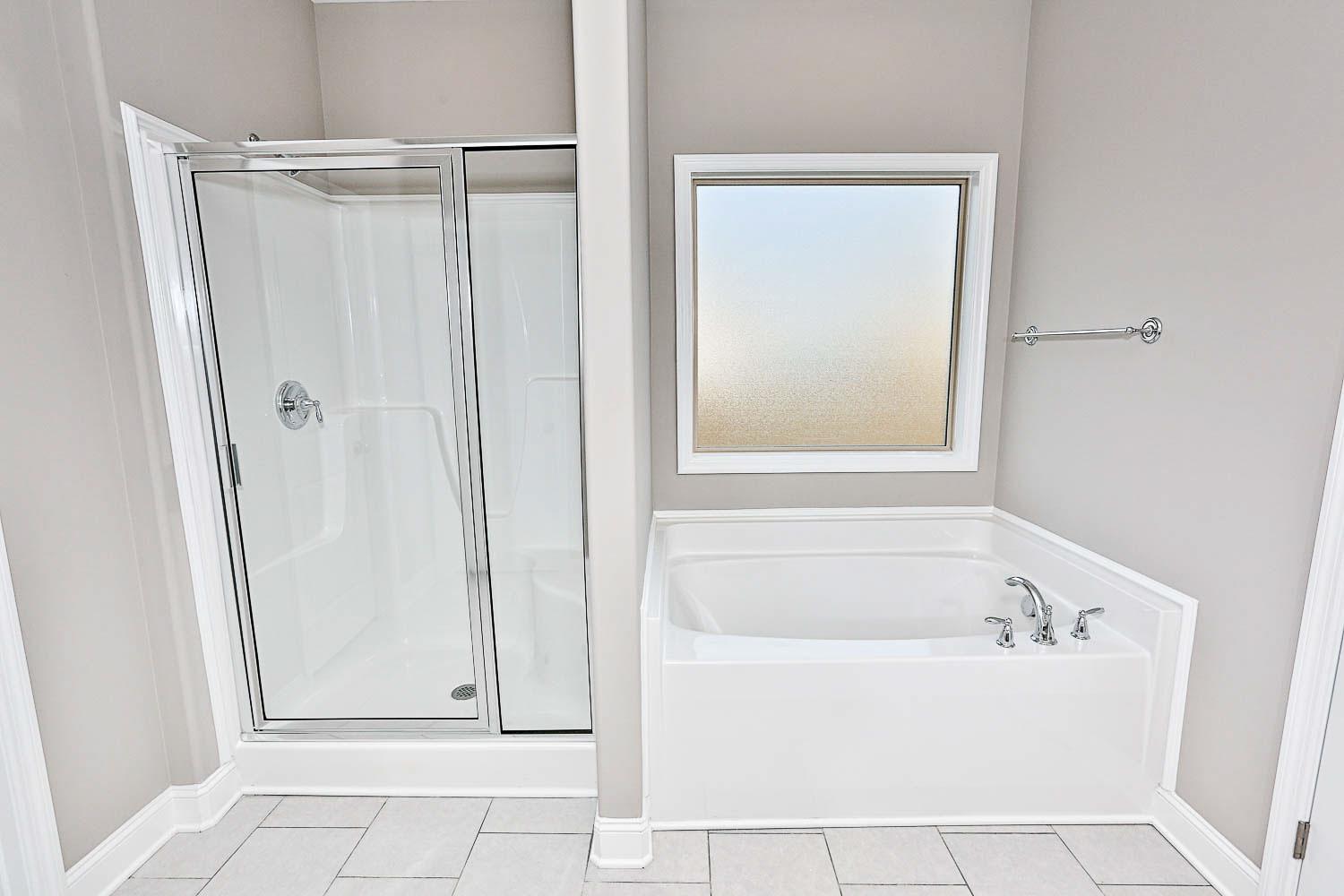 Master bathroom in The Montgomery featuring glass walk-in shower, corner soaking tub, frosted window