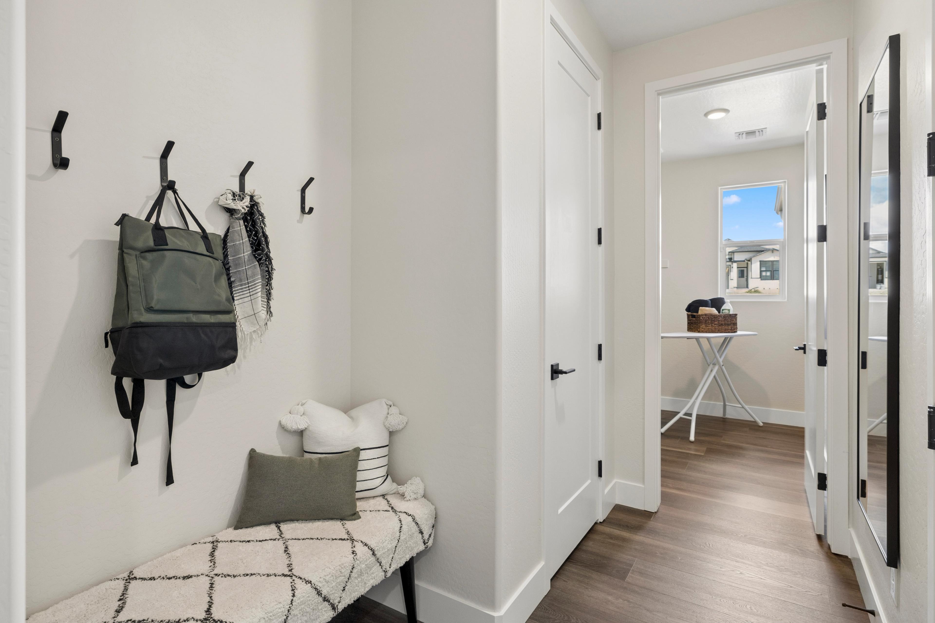 Cozy mudroom entry with wall hooks, green backpack, scarf, cushioned bench and wood floors at South Ranch Western Collection in Prescott AZ