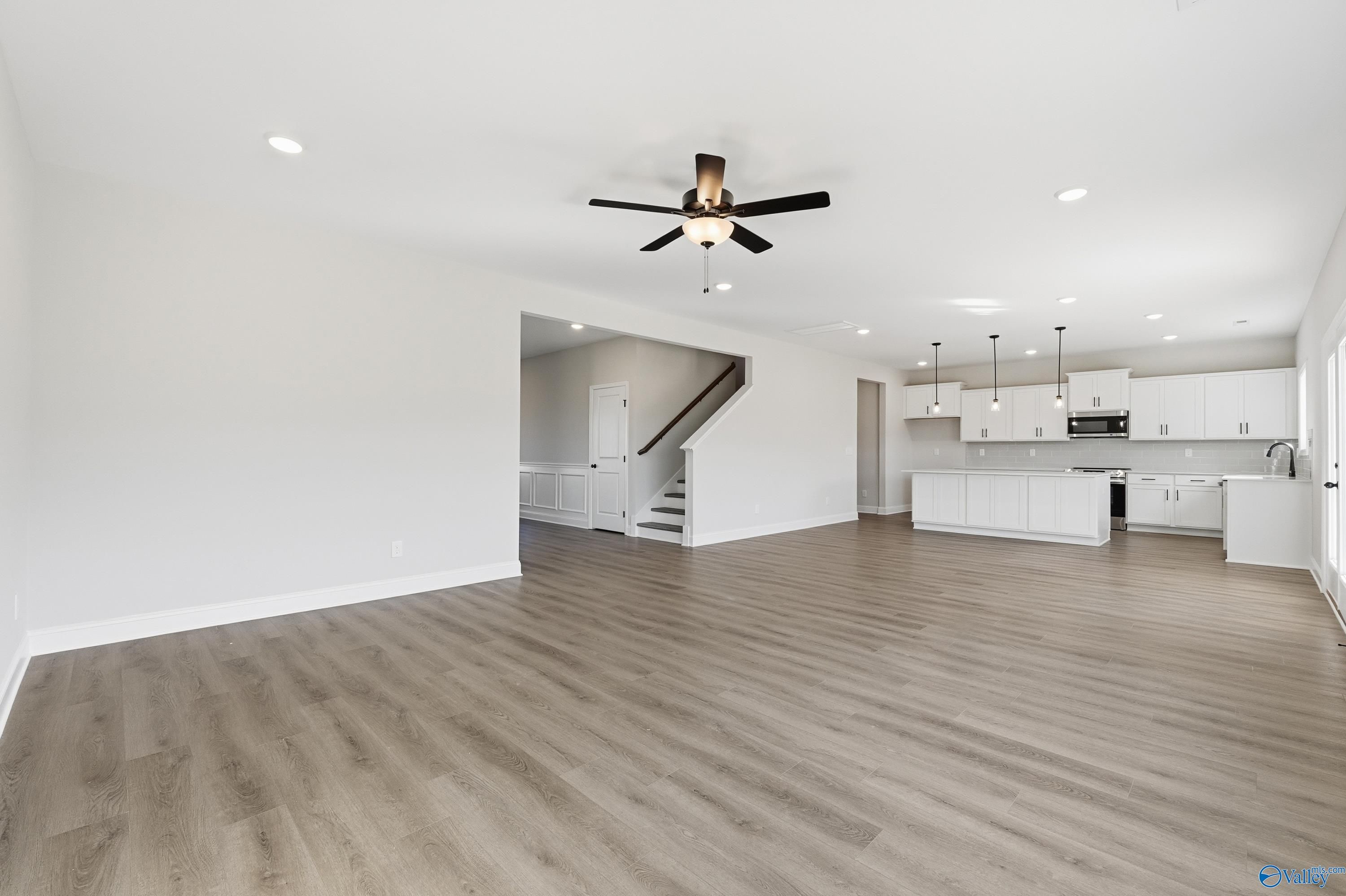 Open-concept living room with modern kitchen, ceiling fan, and light wood laminate floors in Davidson Homes The Chelsea C, Harvest, Alabama