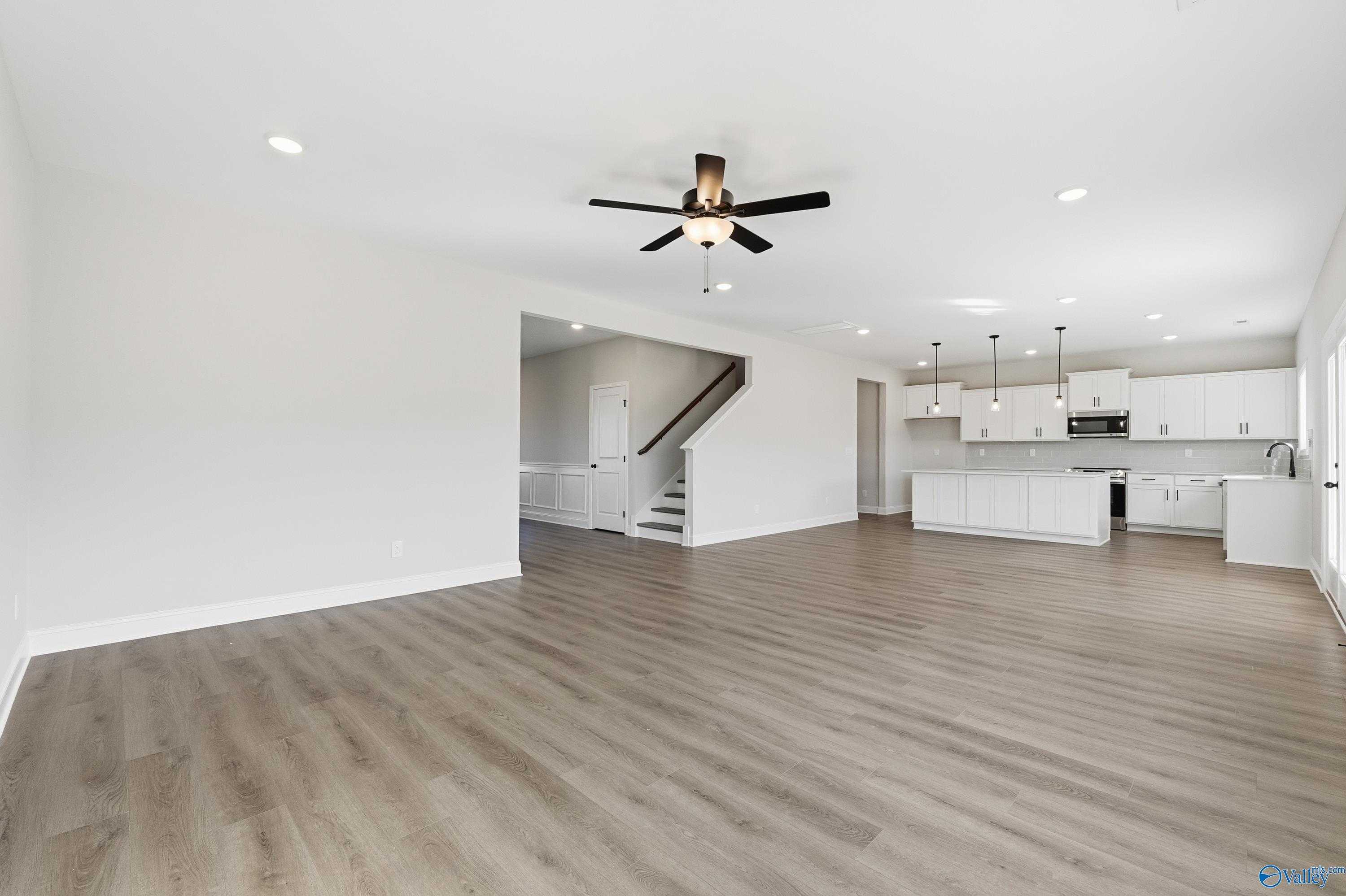 Open-concept living room with modern kitchen, ceiling fan, and light wood laminate floors in Davidson Homes The Chelsea C, Harvest, Alabama