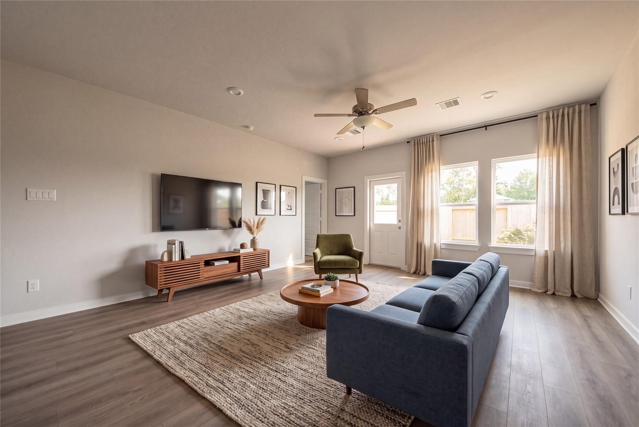 Bright living room with wood-look flooring, blue sofa, and ceiling fan in Davidson Homes' The Blanco E, Dayton, Texas